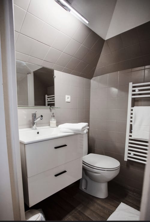Salle de bains moderne avec vasque blanche, toilettes, sèche-serviettes chauffant et carrelage gris à la Résidence Le Roc Fleuri, Saint Malo