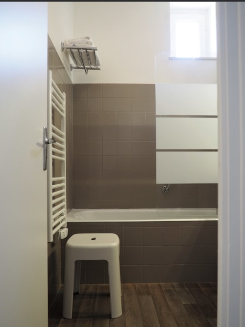 Salle de bain moderne aux murs en carrelage marron, porte-serviettes blanc et sol en bois à la Résidence Le Roc Fleuri, Saint Malo