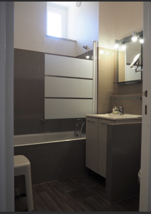 Salle de bain moderne à la Résidence Le Roc Fleuri à Saint Malo avec carrelage foncé, vasque blanche, baignoire, miroir et luminaires