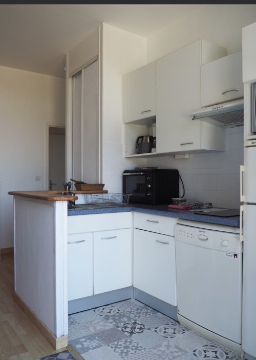 Cuisine moderne blanche avec plan de travail bleu dans un appartement à Saint-Malo, équipée d'une cuisinière, lave-vaisselle et bar en bois