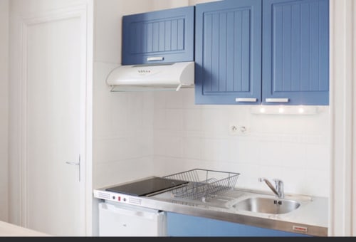 Kitchenette compacte aux armoires bleues, cuisinière, évier et murs blancs à la Résidence Le Roc Fleuri, Saint-Malo