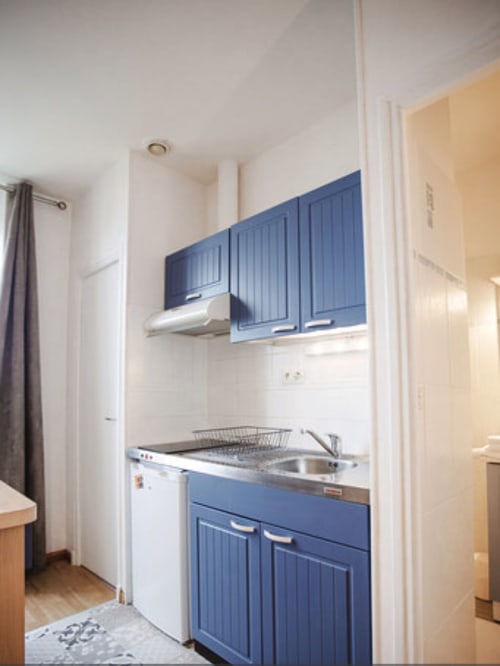 Kitchenette compacte avec meubles bleus, évier en acier inoxydable et électroménagers blancs à la Résidence Le Roc Fleuri à Saint-Malo