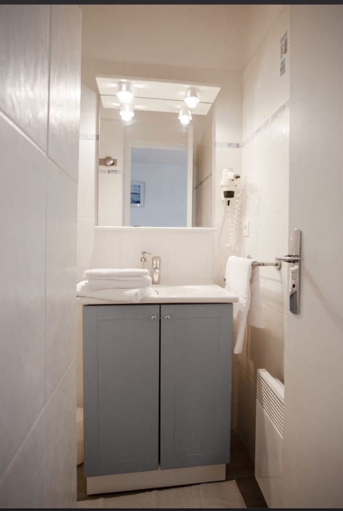 Salle de bains moderne à la Résidence Le Roc Fleuri, Saint Malo avec vanité grise, lavabo blanc, miroir éclairé et serviettes blanches