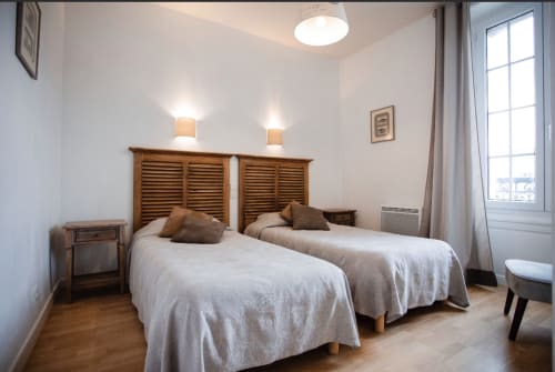 Lits jumeaux aux têtes de lit en bois dans un lumineux appartement de Saint-Malo à la Résidence Le Roc Fleuri, fenêtre avec vue sur mer
