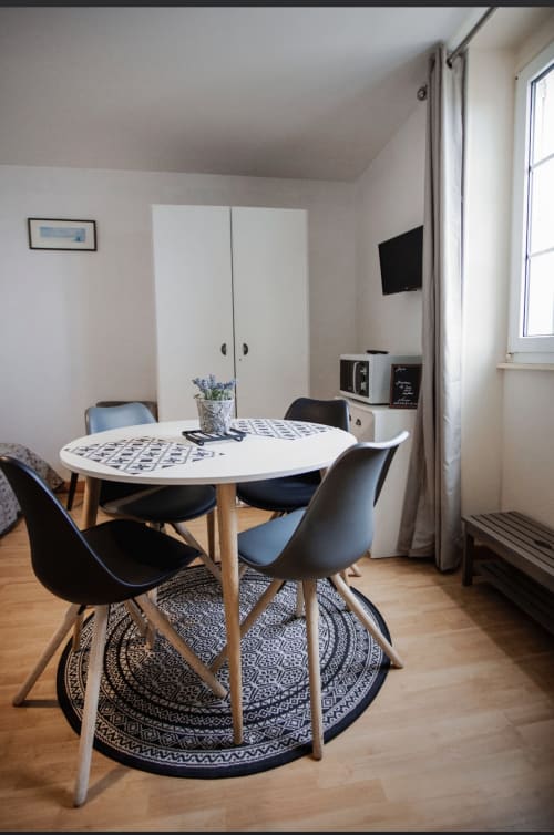 Coin repas moderne dans l'appartement Le Roc Fleuri à Saint-Malo avec table ronde, chaises noires et téléviseur dans une chambre mansardée lumineuse