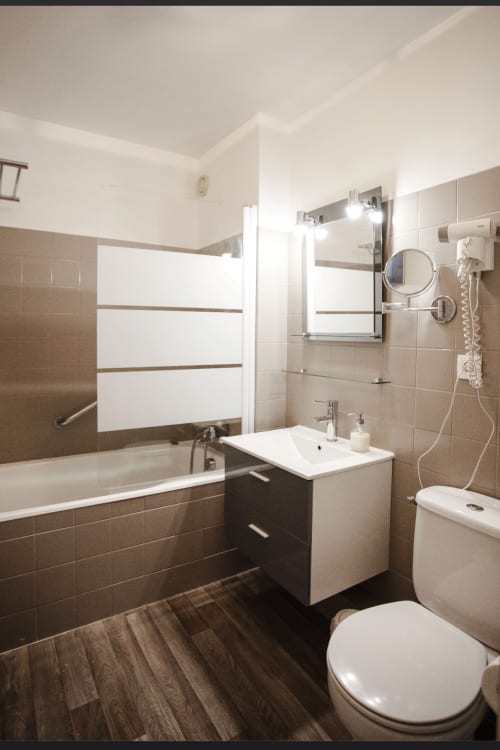 Salle de bains moderne de la Résidence Le Roc Fleuri, Saint-Malo avec carrelage marron, lavabo blanc, toilettes, baignoire et miroir