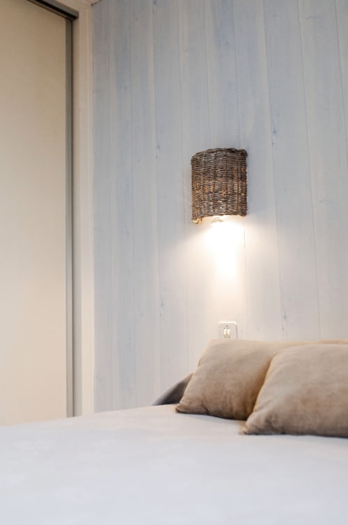 Chambre moderne à la Résidence Le Roc Fleuri à Saint-Malo avec applique murale en rotin au-dessus du lit garni de coussins