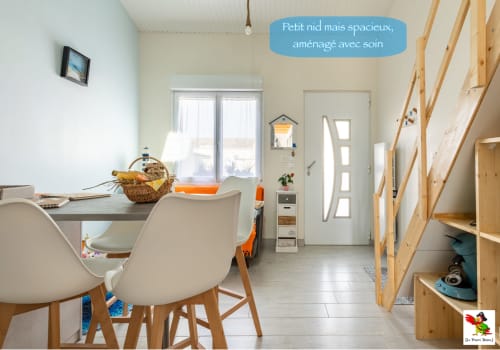 Petit séjour du gîte Le Pirate Benèze avec table à manger, étagères en bois, portes sur jardin et mobilier moderne