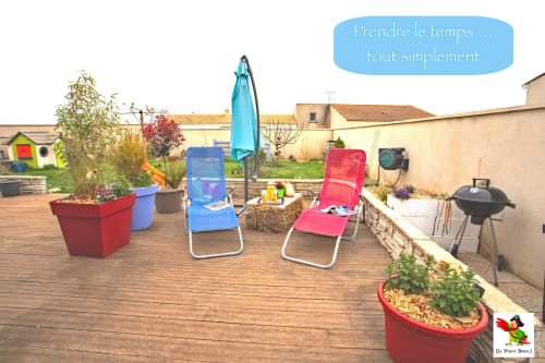 Terrasse ensoleillée du Pirate Benèze avec transats colorés, parasol bleu, jardinières et barbecue à Trizay