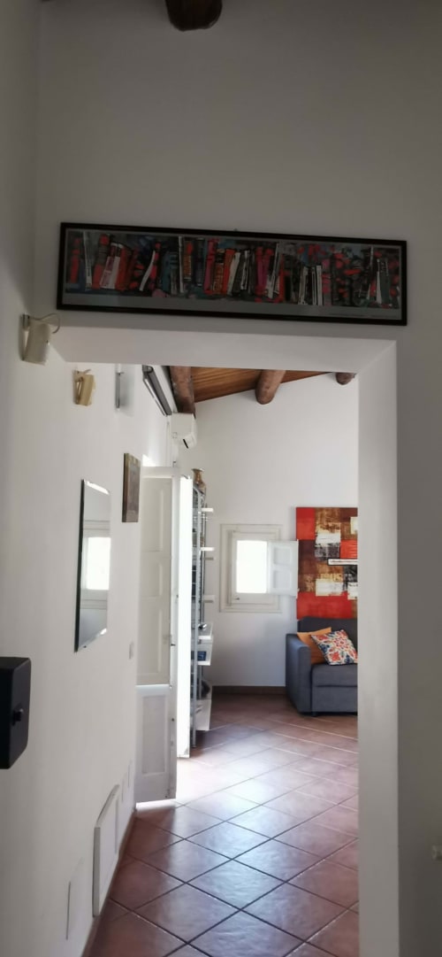 Hallway entry to Attico Apartment at Casa Bellini, Palermo with exposed wooden beam, framed bookshelf, and living area view