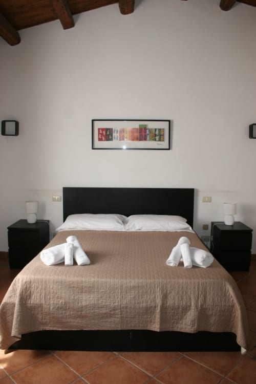 Modern bedroom at Casa Bellini in Palermo with black bed frame, white pillows, beige bedspread, twin nightstands, and