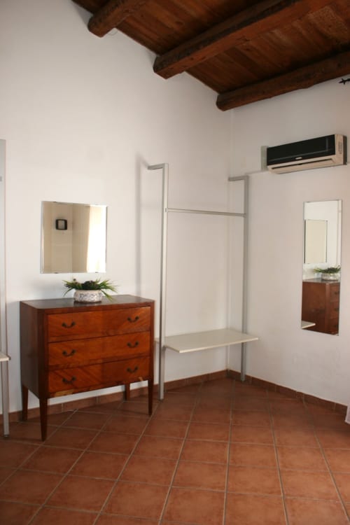 Modern bedroom at Casa Bellini Palermo with wooden dresser, mirrors, metal clothing rack, and terracotta floors