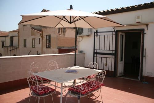 Palermo rooftop terrace at Casa Bellini with dining table, red cushioned chairs, and beige umbrella with city views