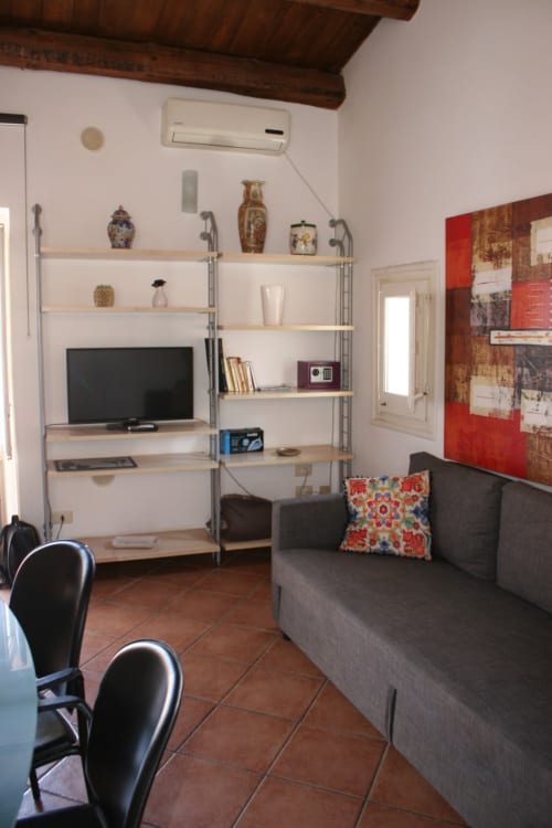 Modern living room at Casa Bellini Palermo with shelving, TV, gray sofa, and terracotta floors in Attico Apartment