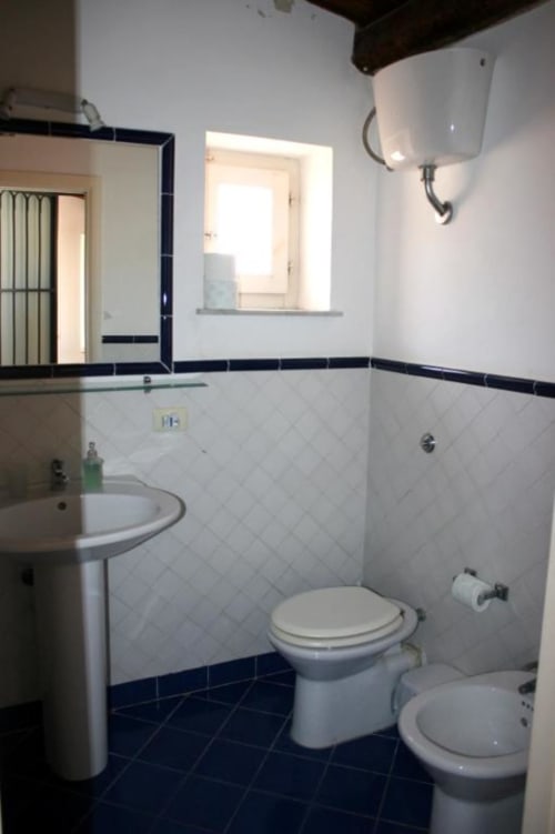 Modern bathroom in Casa Bellini Attico Apartment, Palermo, with white tile walls, dark tile floor, pedestal sink, and toilet