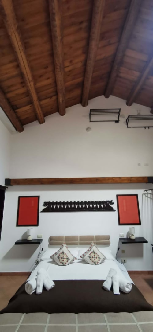 Modern bedroom at Casa Bellini Palermo with exposed wooden beams, red wall art, and white bedding with decorative pillows