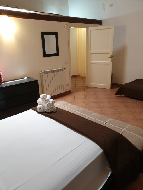 Spacious bedroom at Casa Bellini, Palermo with white linens, rolled towels, dark wood beams, radiator, and terracotta floors