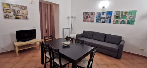 Primo Apartment living room at Casa Bellini in Palermo with dining table, black sofa, TV, and colorful wall art