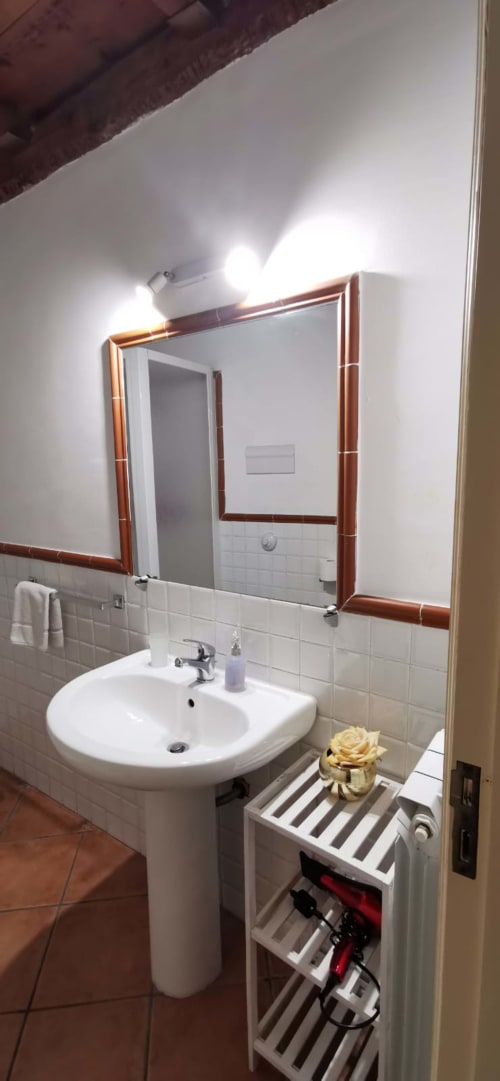 Modern bathroom at Casa Bellini in Palermo with pedestal sink, wall-mounted mirror with wooden frame, white tile backsplash,