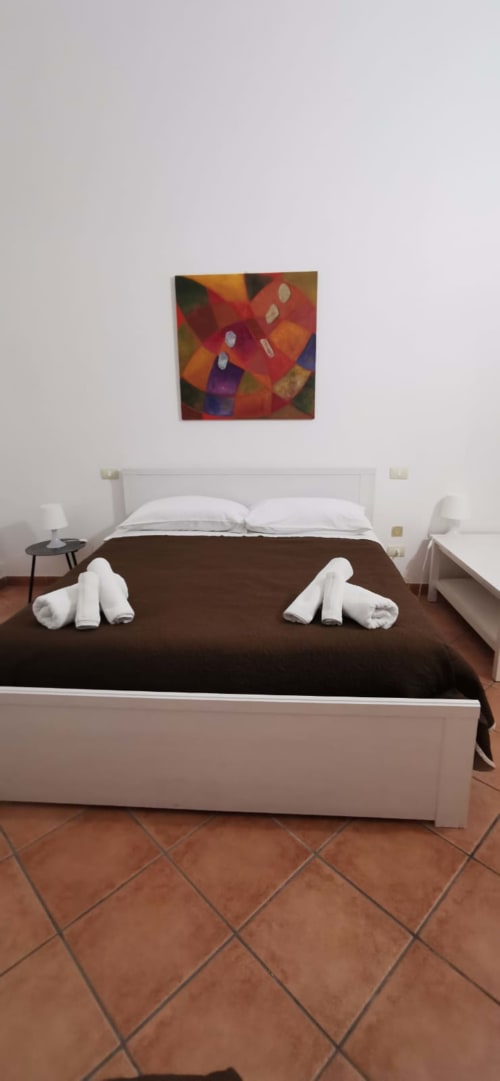 Modern bedroom at Casa Bellini in Palermo with white bed, brown linens, colorful artwork, and terracotta tile floor