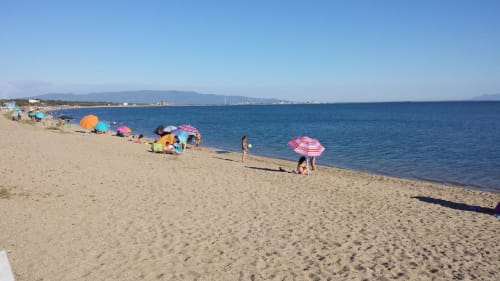 Spiaggia sabbiosa a Torre Grande Oristano con ombrelloni colorati, mare blu cristallino e costa lontana