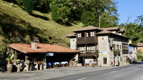 Hotel Rural Los Texos, construcción de piedra tradicional con tejado de tejas rojas, ubicado en las exuberantes montañas verdes de La Riera de Covadonga