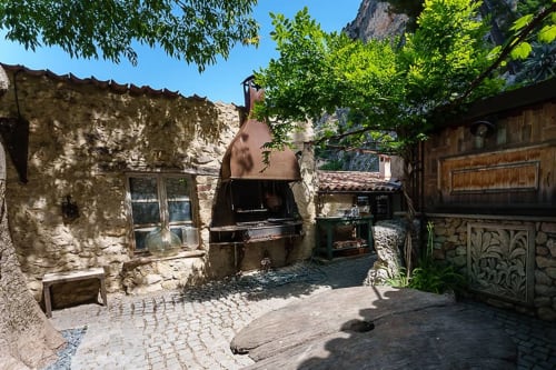 Rustikaler Innenhof von La Bouscatière in Moustiers-Sainte-Marie mit Steingebäuden, Grill, Grün und französischem Dorfcharme