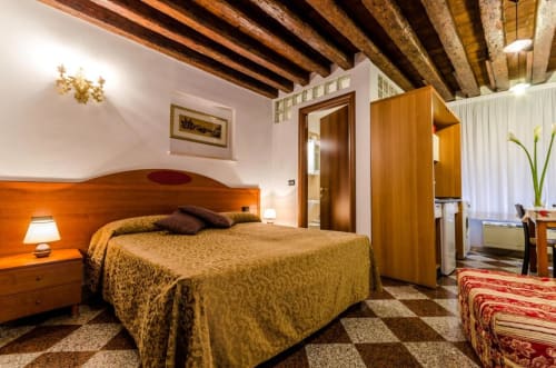 Camera con travi in legno dell'Hotel Ariel Silva Venice Apartments con copriletto dorato, travi a vista e piastrelle a quadri