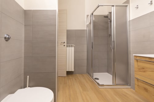 Modern bathroom with gray tile walls, wooden flooring, glass shower enclosure, toilet, and vanity at B&B La Camia in Castel