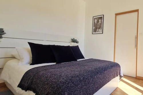 Chambre moderne à la Conciergerie Des Climats à Beaune avec lit queen-size, oreillers noirs, plaid foncé et porte en bois.