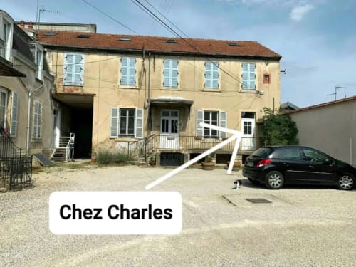 Façade jaune de l'appartement Chez Charles à Beaune, avec volets bleus et zone de stationnement