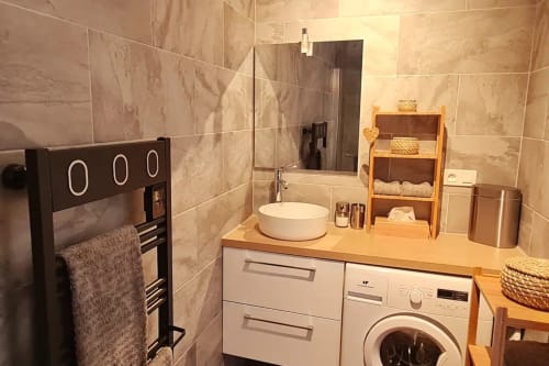 Salle de bain moderne à la Conciergerie Des Climats à Beaune avec lavabo blanc, lave-linge, sèche-serviettes chauffant et murs carrelés.