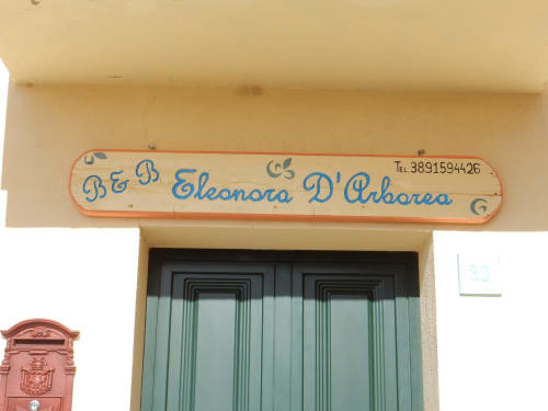 Insegna della struttura B&B Eleonora D'Arborea a Posada, Italia con persiane verdi e dettagli di contatto