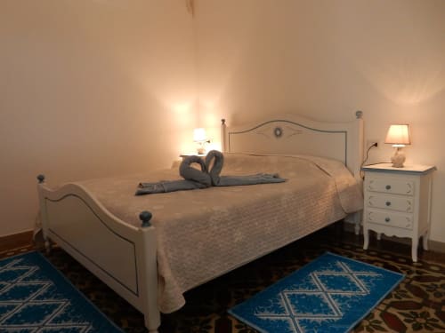 Camera accogliente presso B&B Eleonora D'Arborea a Posada con letto color crema, comodini, lampade e tappeti blu.
