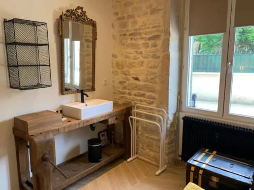 Salle de bain rustique d'un appartement à Beaune avec meuble vasque en bois, murs en pierre, miroir et équipements modernes