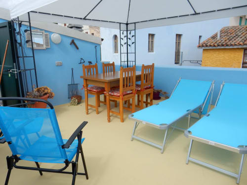 Cortile esterno del B&B Eleonora D'Arborea a Posada con lettini blu, tavolo in legno e area salotto coperta