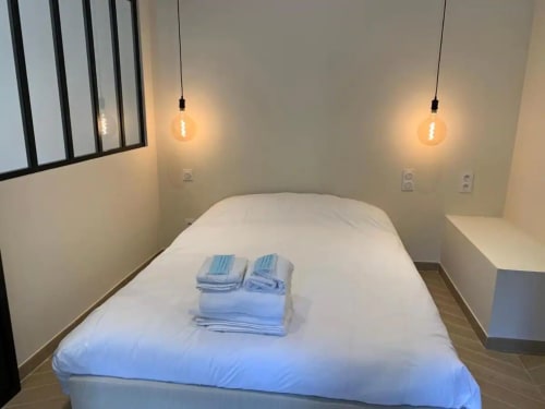 Chambre moderne à la Conciergerie Des Climats à Beaune avec lit blanc, draps bleus, luminaires suspendus et décoration minimaliste