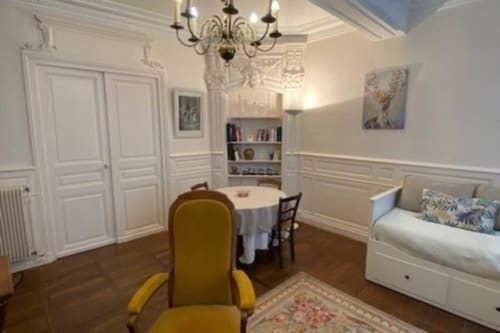 Élégant appartement de Beaune avec fauteuil jaune, table ronde, lit de jour blanc et lustre classique dans le salon