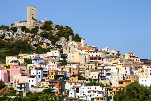 Colorful hillside village of Posada, Italy with medieval tower overlooking pastel buildings