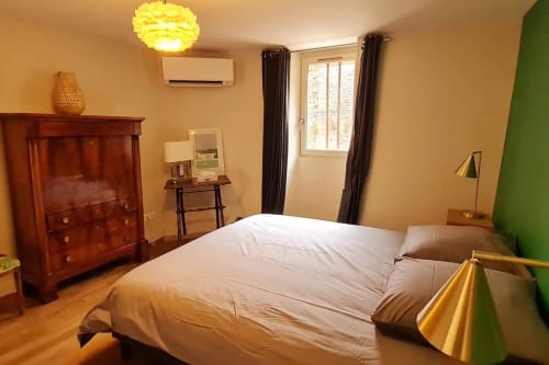 Chambre moderne à la Conciergerie Des Climat à Beaune avec lit blanc, mobilier en bois, mur d'accent vert et suspension jaune