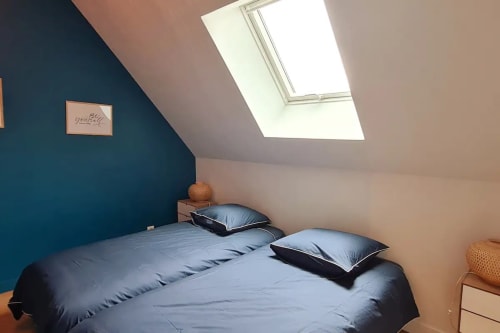 Chambre mansardée à la Conciergerie Des Climats à Beaune avec lucarne, mur d'accent bleu-vert et literie bleue