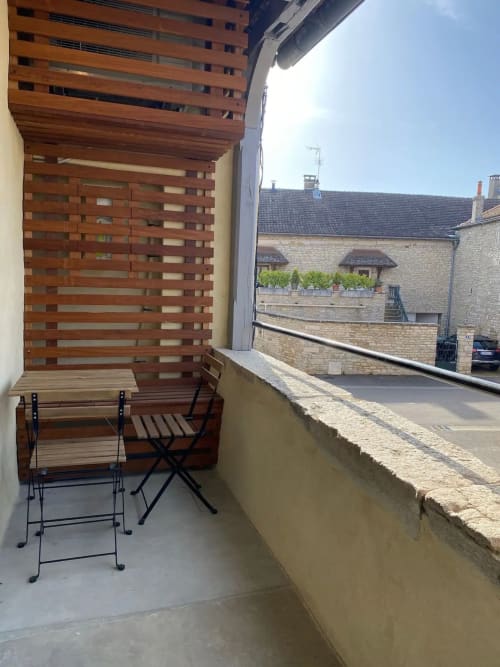Zone de détente en balcon à la Conciergerie Des Climats à Beaune avec chaises en bois, claustra à lames et vue sur la ville historique