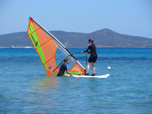 Windsurfista in acque turchesi presso Posada, Italia con vela colorata arancione e verde con sfondo montuoso