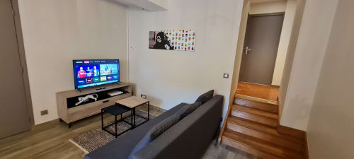 Salon moderne d'un appartement à Beaune avec télévision, canapé foncé, parquet et accès à la chambre