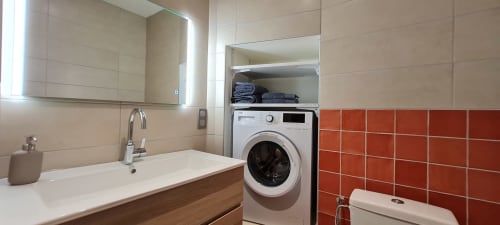 Salle de bain moderne à l'appartement Conciergerie Des Climats à Beaune, avec lavabo, lave-linge, mur accent en carrelage rouge et miroir