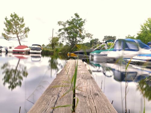Ponton en bois s'avançant dans les eaux calmes de Villa Eden Bleu à Biscarrosse, avec bateaux amarrés et reflets d'arbres