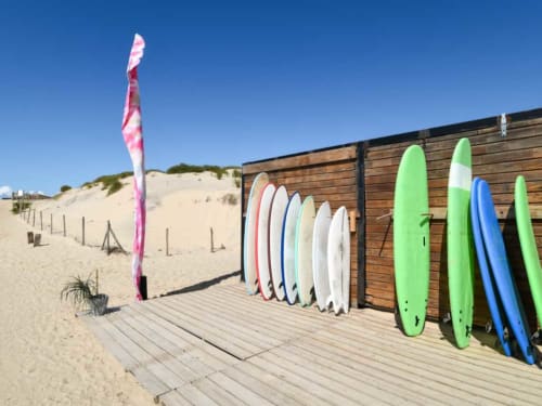 Planches de surf colorées et équipements de planche à voile exposés sur la terrasse en bois de la plage Villa Eden Bleu à Biscarrosse