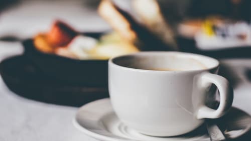 Tasse en céramique blanche avec café sur soucoupe à l'hôtel Mapé à Dampierre-en-Burly, France, avec éléments de petit-déjeuner en arrière-plan