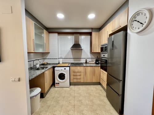 Cocina moderna en Apartamentos J&A Terrassa con muebles de madera, electrodomésticos de acero inoxidable y azulejos blancos