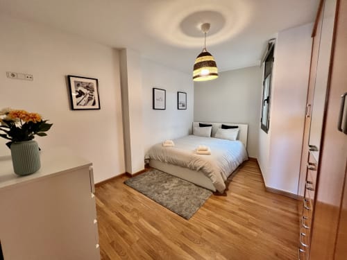 Dormitorio moderno en Apartamentos J&A en Terrassa con cama queen, suelos de madera, lámpara colgante y decoración minimalista